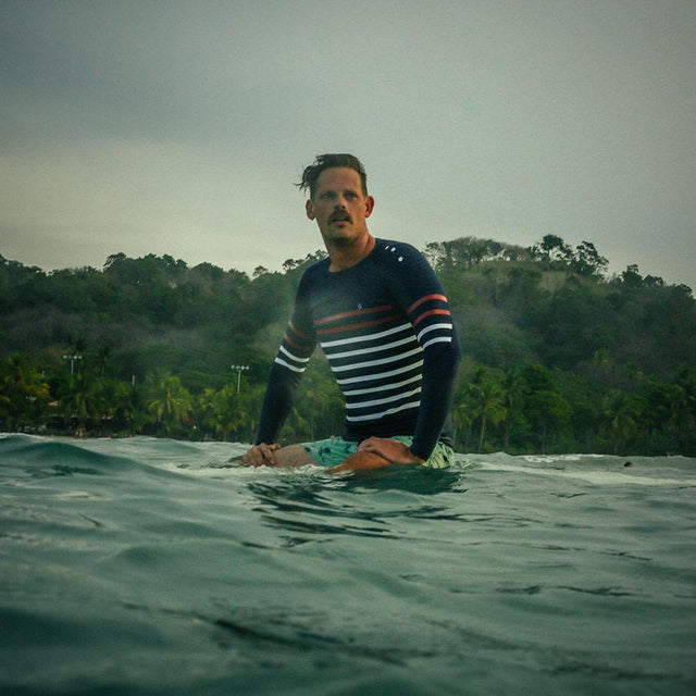 Homme assis sur sa planche de surf en top néoprène noé 